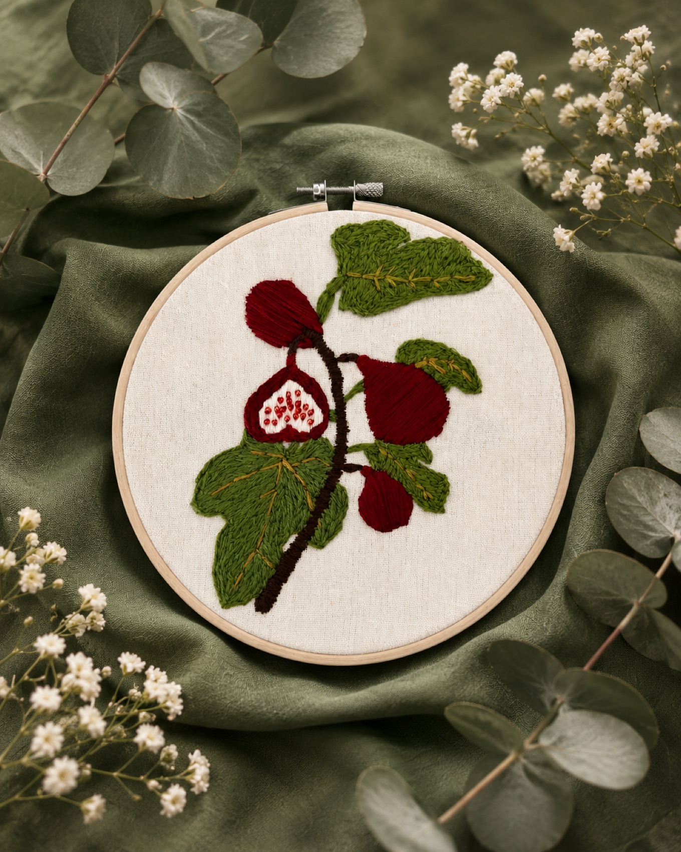 A branch of figs and leaves, hand-embroidered in greens and deep red.