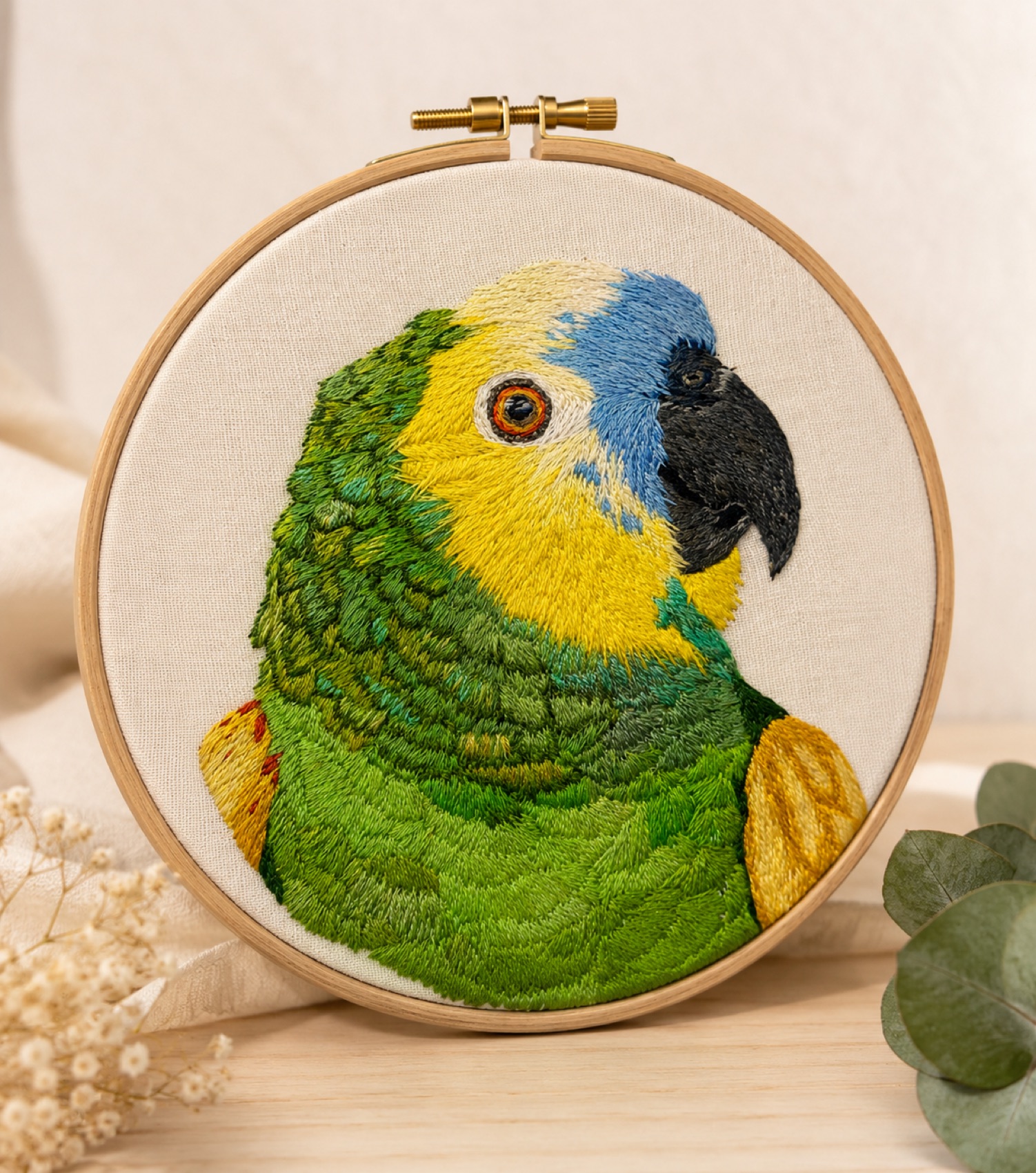A vibrant green Amazon parrot hand-embroidered in long-and-short stitch, with red and blue wing flashes.